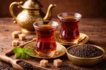 كوبان من الشاي الأسود المحضّر في أكواب زجاجية تقليدية مع أوراق شاي جافة على طاولة خشبية