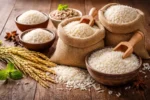 أنواع مختلفة من الأرز الأبيض وحبوب الأرز الخام موضوعة في أوعية وأكياس على سطح خشبي