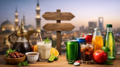 مقارنة بصرية بين مشروبات محلية ومشروبات مستوردة على طاولة خشبية بخلفية مدينة سعودية
